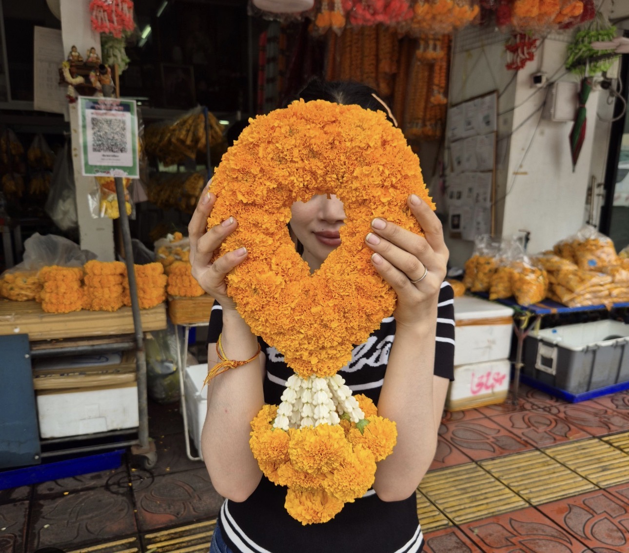 Hand-held Thai marigold garland of bright orange Dao Rueang at a local flower market stall