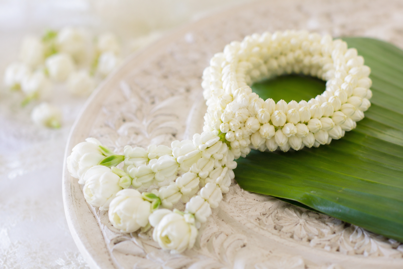 Traditional Thai garland made from fresh white jasmine buds resting on a green banana leaf