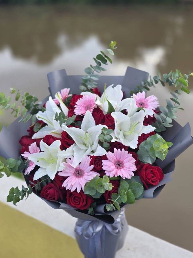 Mixed bouquet with pink gerberas, white lilies, and red roses wrapped in charcoal paper